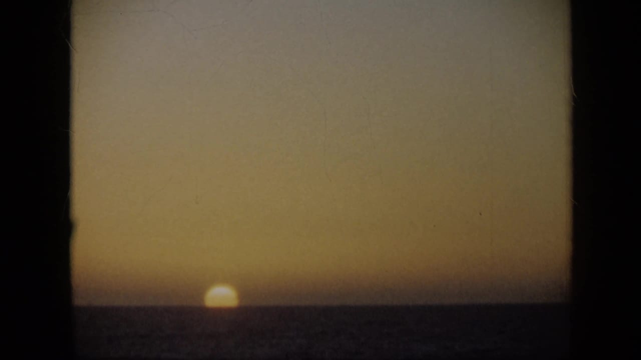 1959 Venezuela home-movie frame with the sun partly below the sea horizon and warm faded color across the sky.