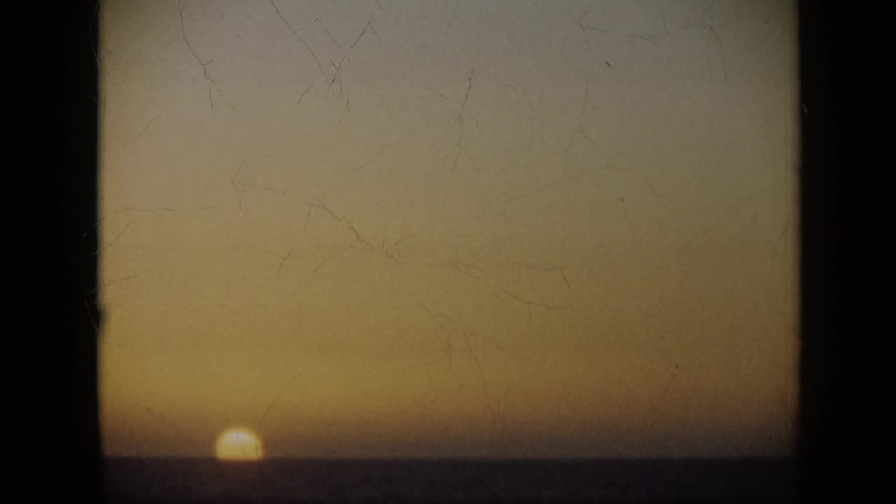 1959 Venezuela 8mm frame showing the sun low on the sea horizon under a warm amber dusk sky with visible film wear.