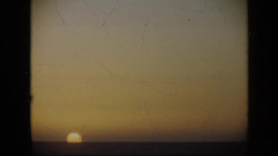 1959 Venezuela 8mm frame showing the sun low on the sea horizon under a warm amber dusk sky with visible film wear.