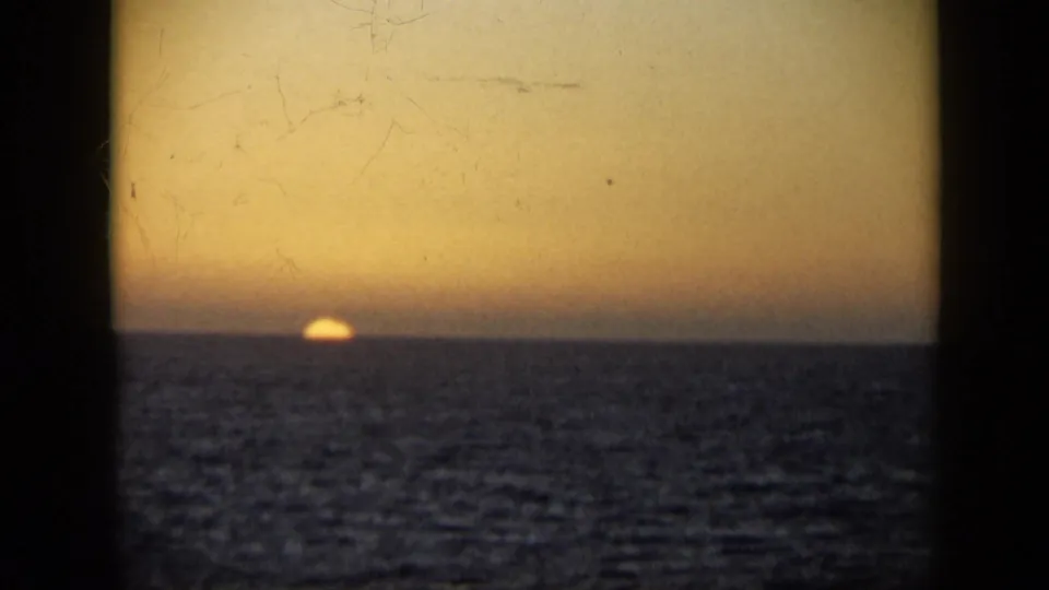 1959 Venezuela 8mm frame showing the sun nearly meeting the sea horizon beneath an amber sky and visible film scratches.