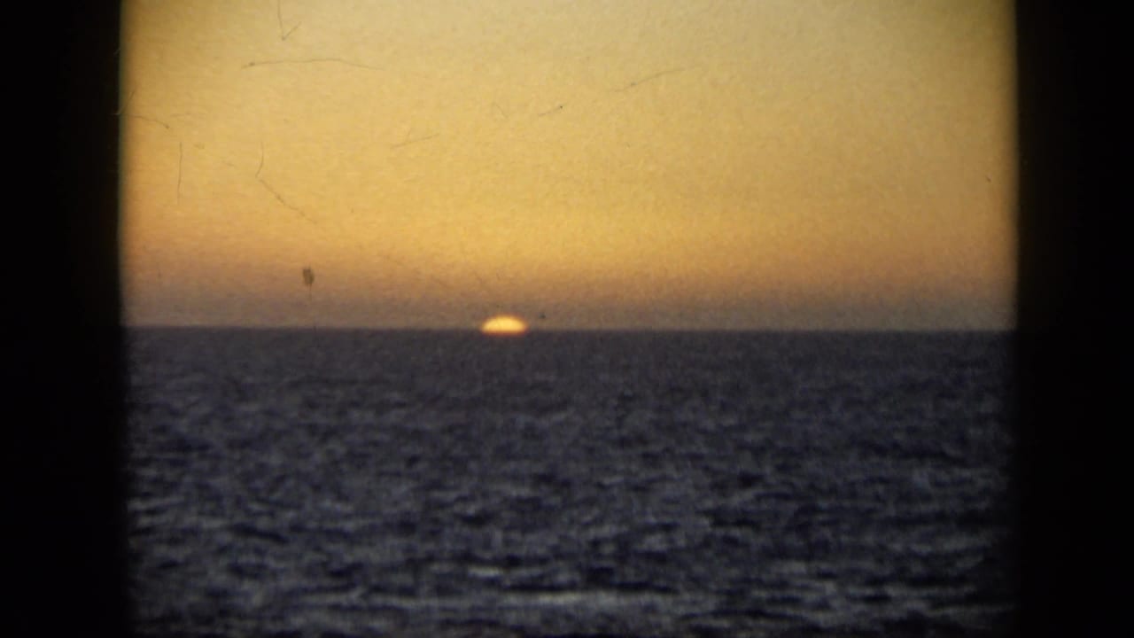 1959 Venezuela 8mm frame with the sun almost set on the sea horizon, warm sky, rippled water, and aged film texture.