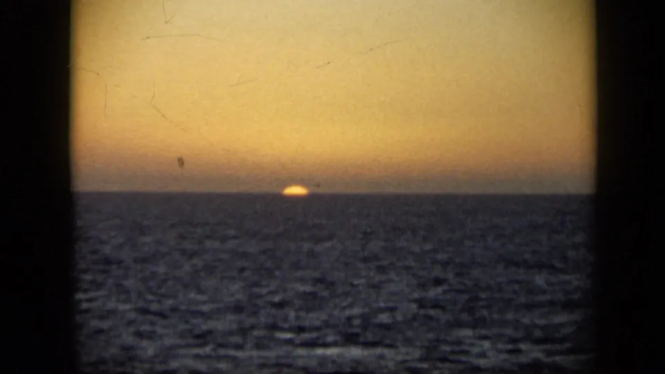 1959 Venezuela 8mm frame with the sun almost set on the sea horizon, warm sky, rippled water, and aged film texture.