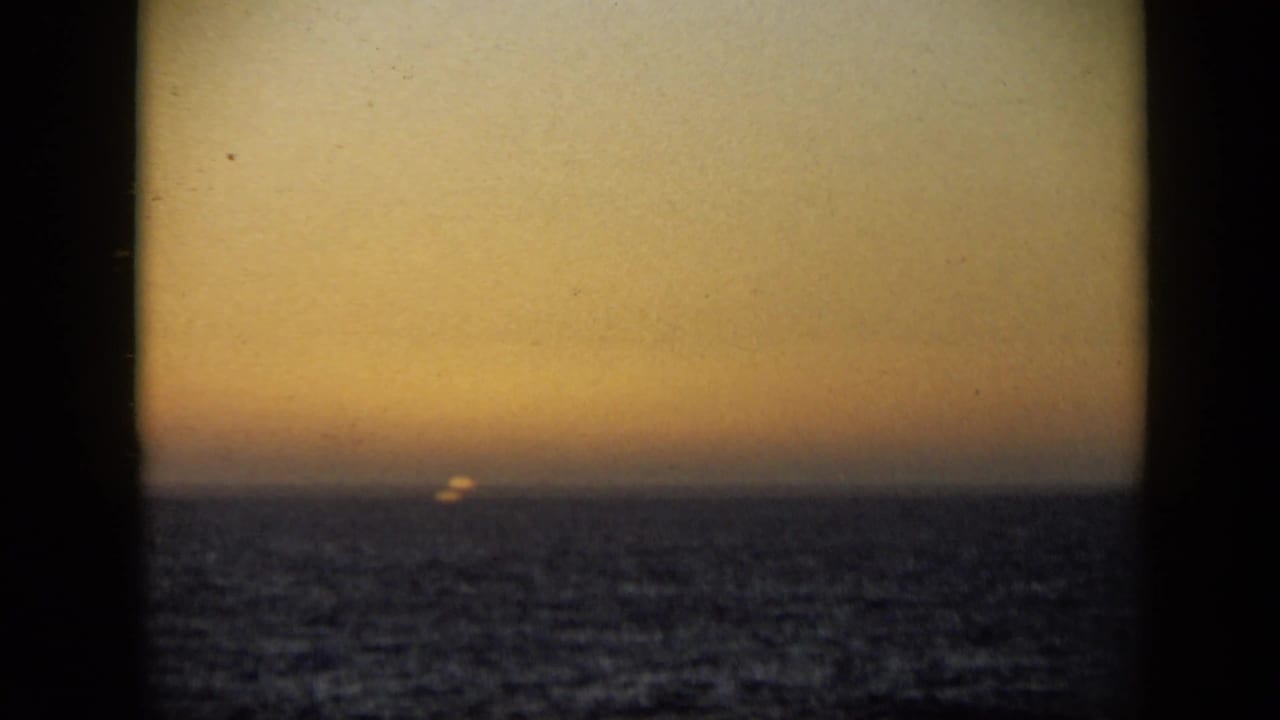 Small sun at the horizon over rippled ocean beneath a hazy amber sky.