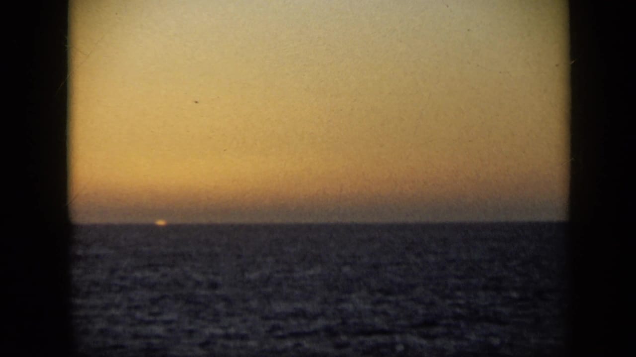 Late-1950s 8mm travel footage shows the sun nearly gone at the horizon over a dark, textured tropical sea.