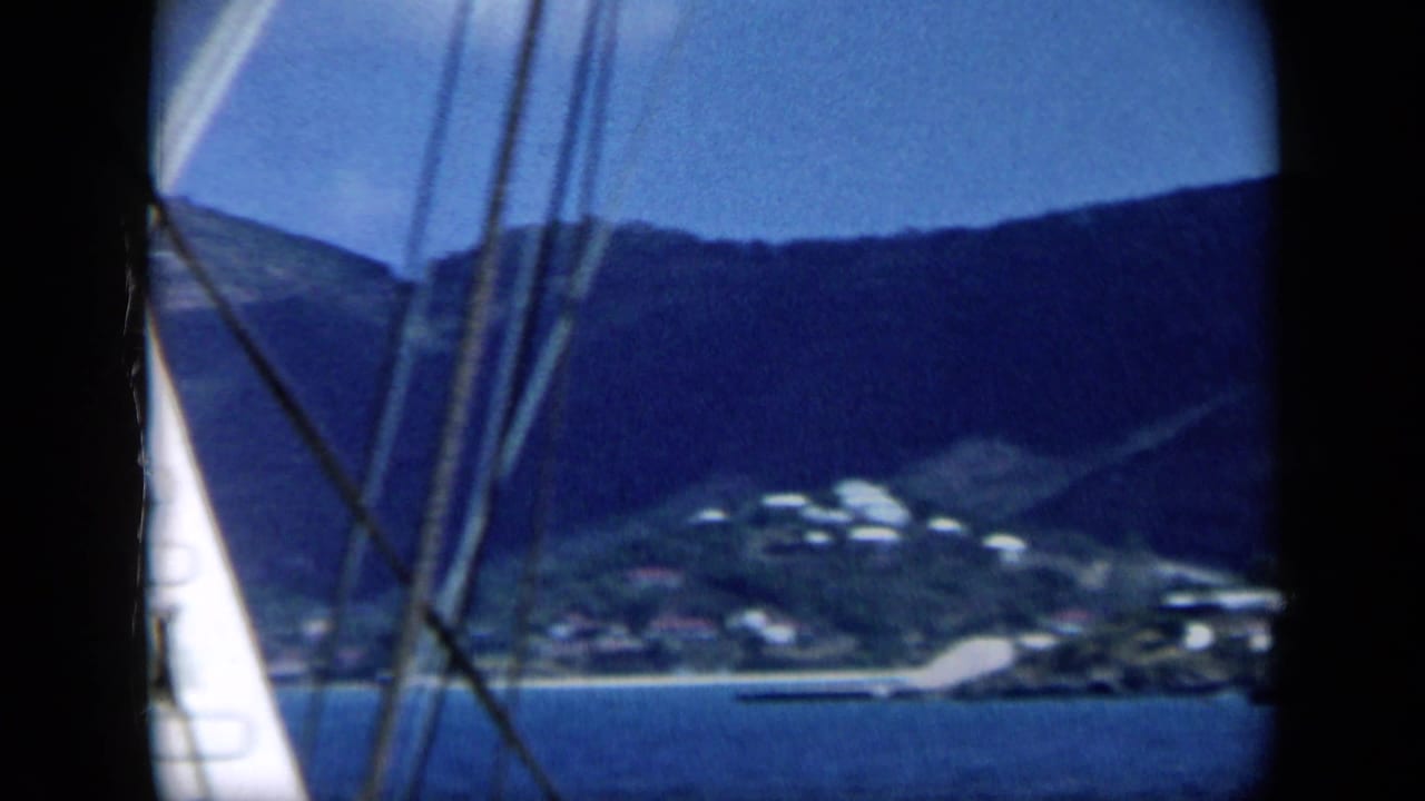 A soft 1959 Venezuela boat shot shows rigging and a white ladder before blue water, a coastal hillside, and small shoreline structures.