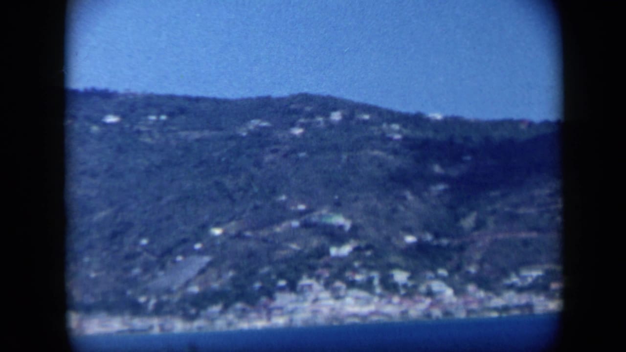 Distant seaside town sits below green hills across blue water.