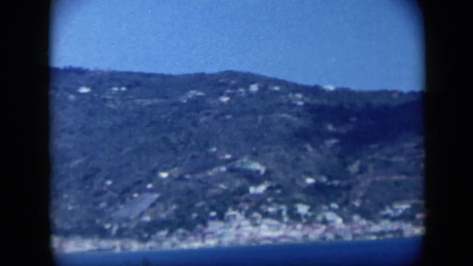 1959 Venezuela coastal view showing a distant town along the shoreline beneath green hills.