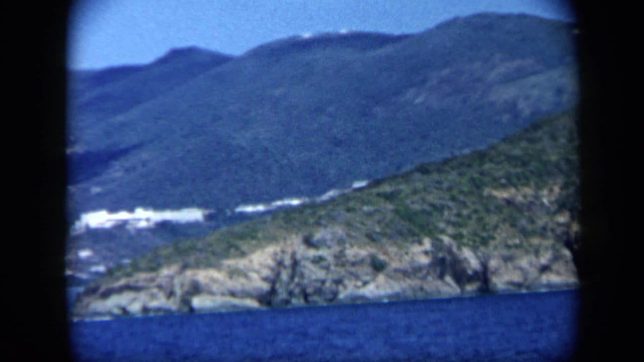 1959 Venezuela 8mm view of rocky coastal land, green slopes, blue sea, and distant mountains.