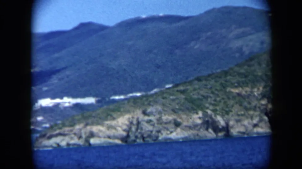 1959 Venezuela 8mm view of rocky coastal land, green slopes, blue sea, and distant mountains.