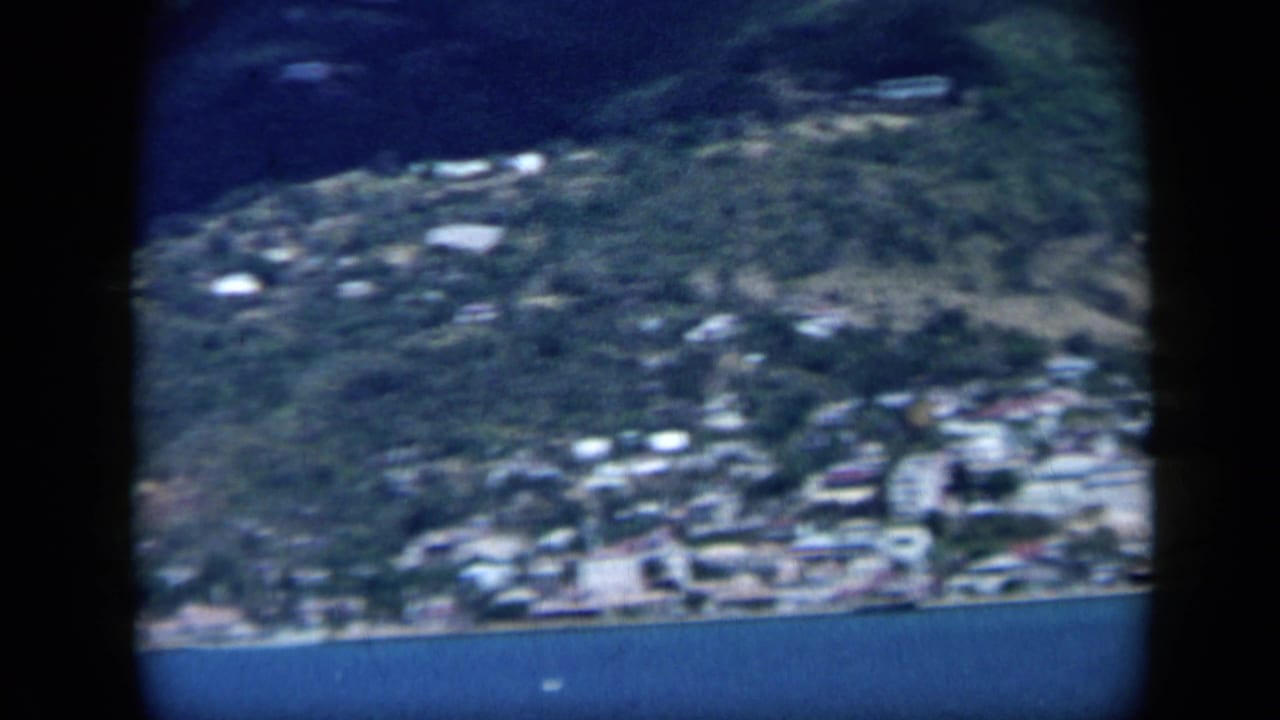 1959 Venezuela coastal view showing a hillside town and shoreline seen across blue water on 8mm film.