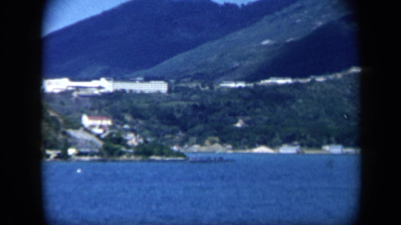 White hillside buildings overlooking blue water and wooded mountainside.