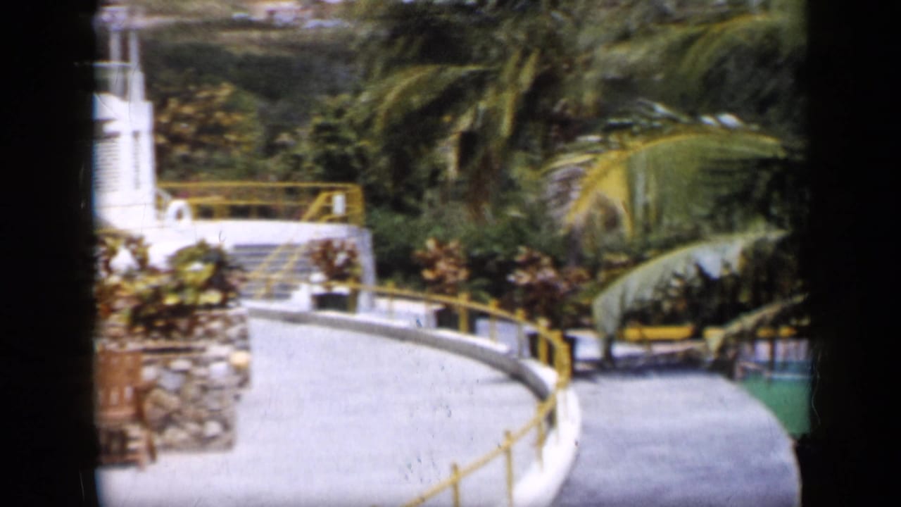 A white courtyard path with yellow railings and palm trees appears in 1959 Venezuela footage.