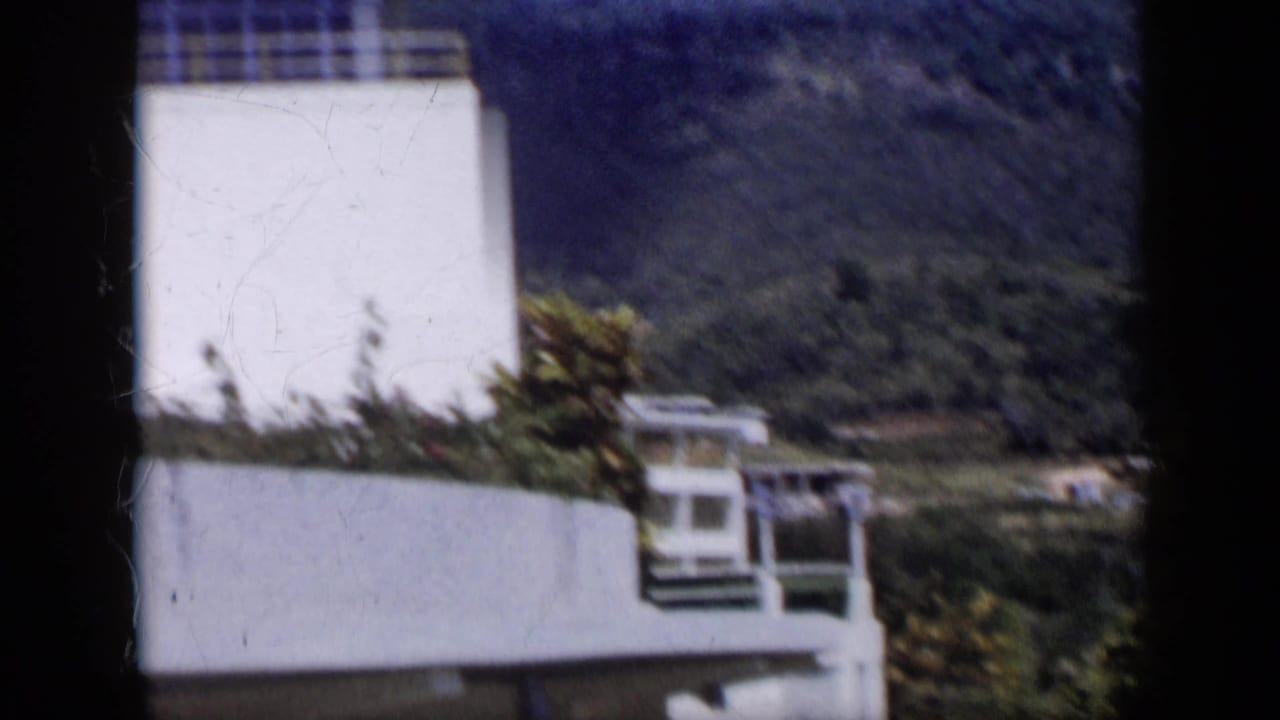 A white modern exterior with garden planting stands before green hills in 1959 Venezuela.