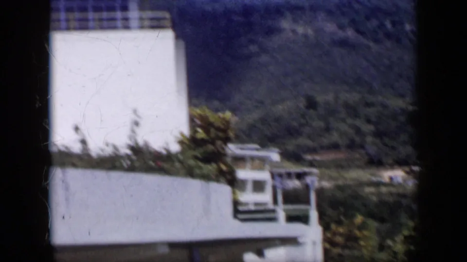 A white modern exterior with garden planting stands before green hills in 1959 Venezuela.
