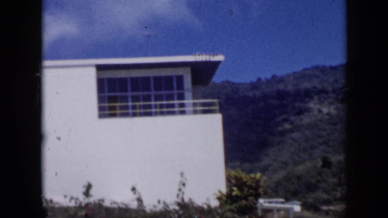 White modernist building facade with large windows, hillside, and blue sky.