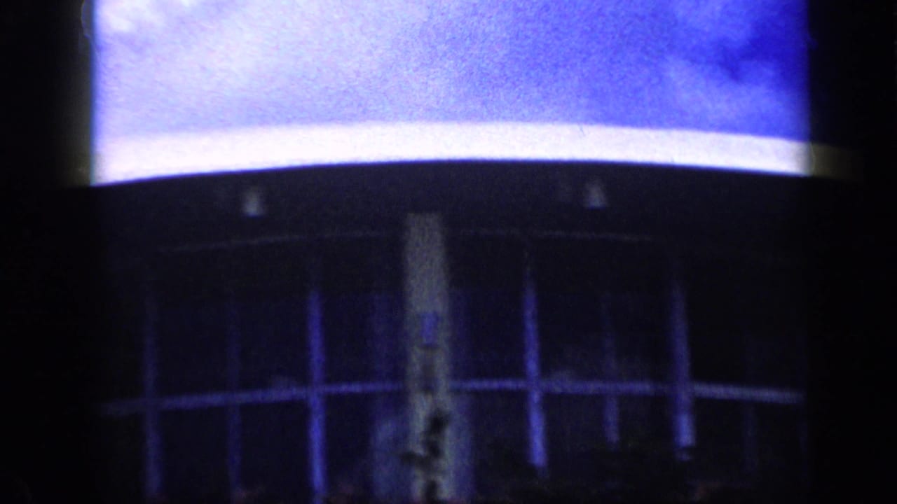 1959 Venezuela 8mm frame with a closer, soft-focus view of the curved canopy, central column, dark window bays, and landscaped plants.