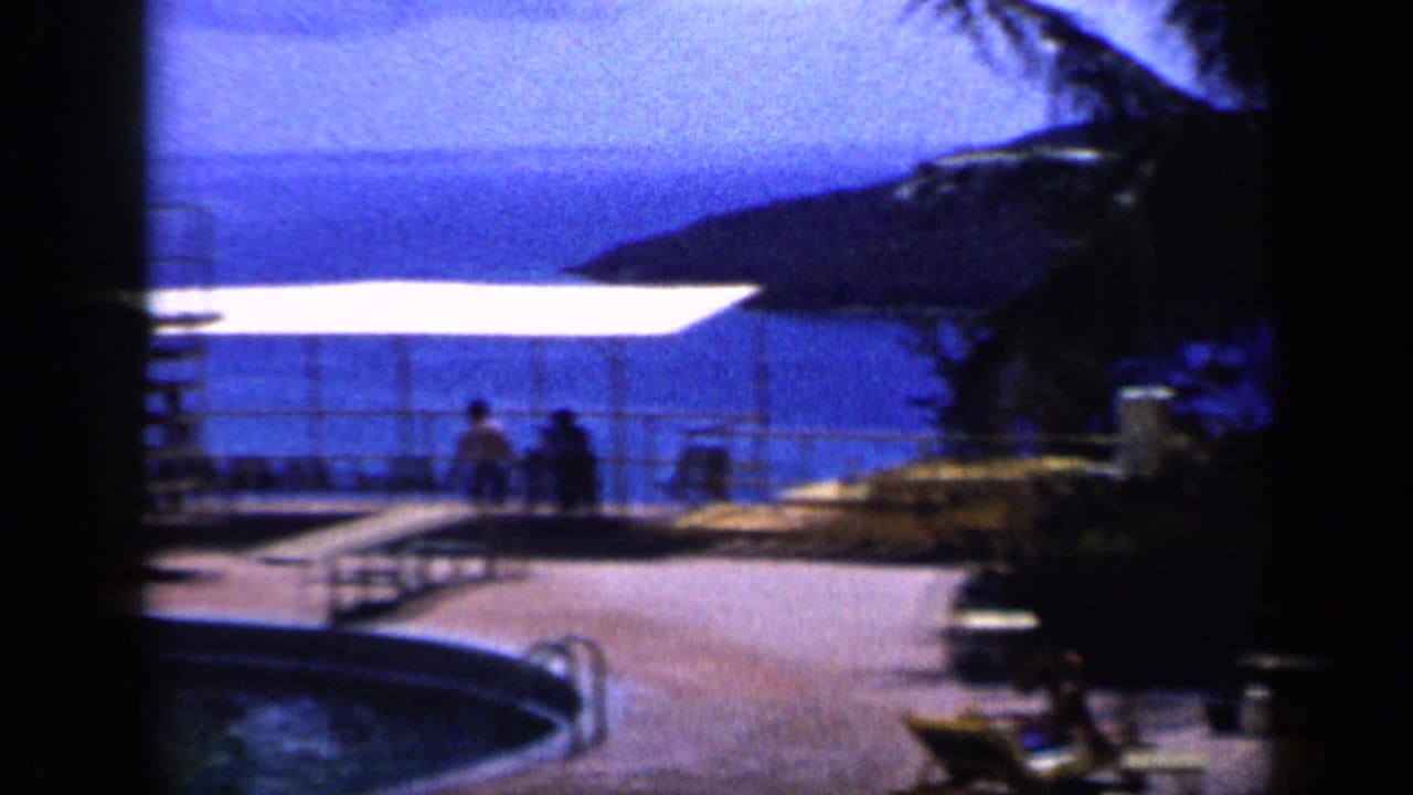 Poolside deck with cabana shade, people, ocean and island hills beyond.