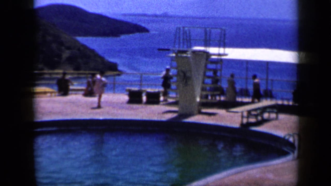 1959 Venezuela poolside scene with a diving platform, scattered guests, lounge seating and coastal water behind the deck.