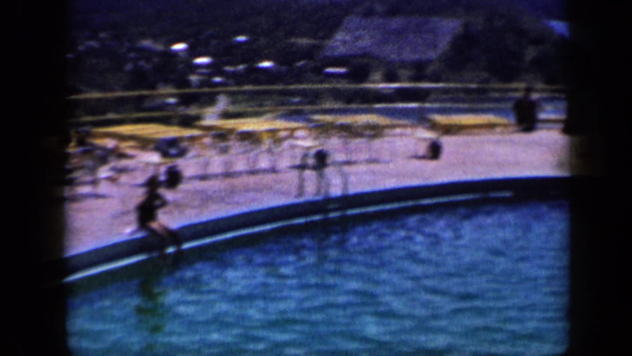 Blue-tinted 1959 Venezuela home-movie frame of a pool edge, lounge chairs, guests and sunlit deck activity.