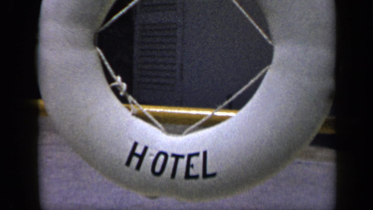 White HOTEL buoy-style sign on a golden pole, seen in 1959 Venezuela travel footage with a dark shaded background.