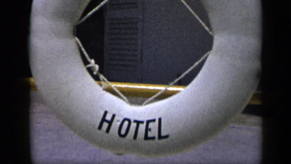 White HOTEL buoy-style sign on a golden pole, seen in 1959 Venezuela travel footage with a dark shaded background.