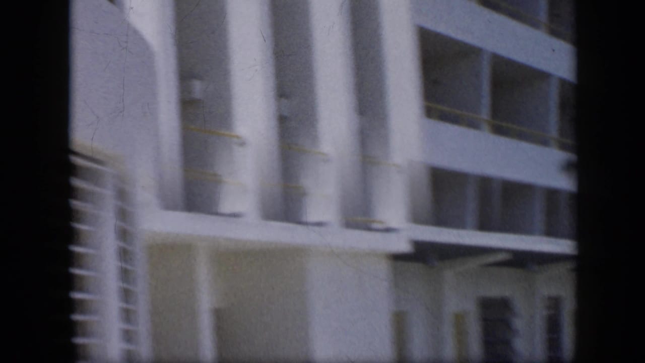 Soft 1959 Venezuela frame showing the lower levels of a white building with columns, balcony openings, and an entrance zone.