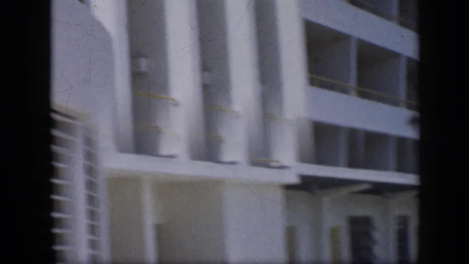 Soft 1959 Venezuela frame showing the lower levels of a white building with columns, balcony openings, and an entrance zone.