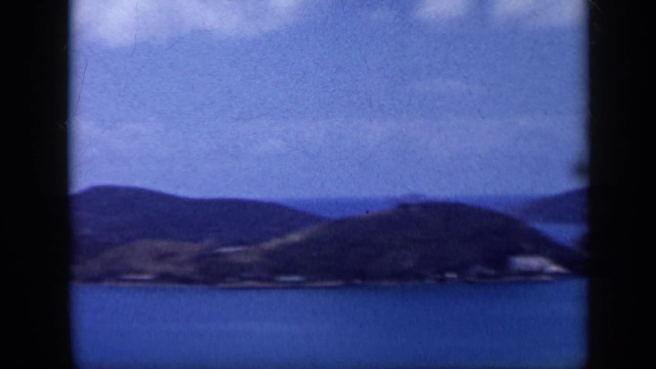 1959 Venezuela home-movie frame showing a blue bay below rolling hills, with soft focus and dark 8mm frame borders.