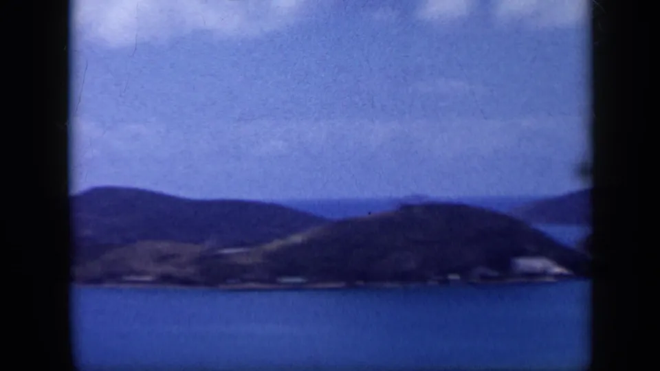 1959 Venezuela home-movie frame showing a blue bay below rolling hills, with soft focus and dark 8mm frame borders.