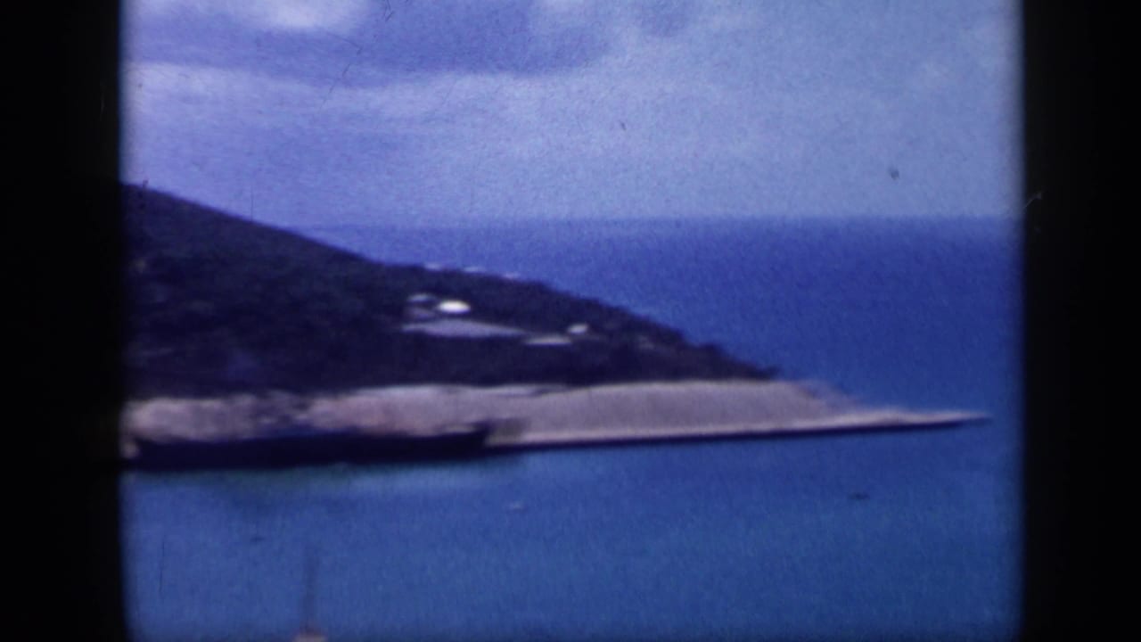Final 1959 Venezuela frame shows a coastal hill above a pale shoreline strip, surrounded by blue bay water.