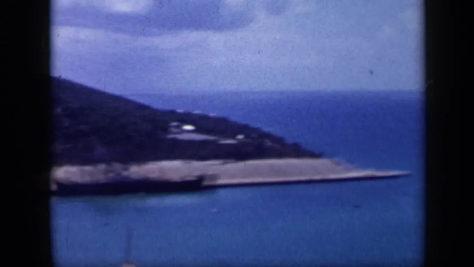 Final 1959 Venezuela frame shows a coastal hill above a pale shoreline strip, surrounded by blue bay water.