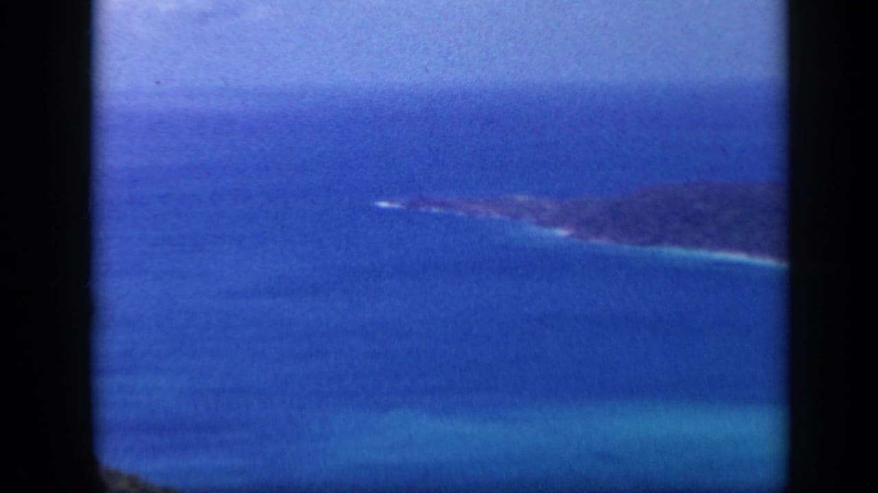 Distant forested island coastline across deep blue ocean and turquoise shallows.