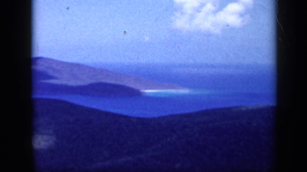 1959 Venezuela 8mm frame showing distant sea, layered headlands or islands, dark foreground hills, and bright clouds above the coast.