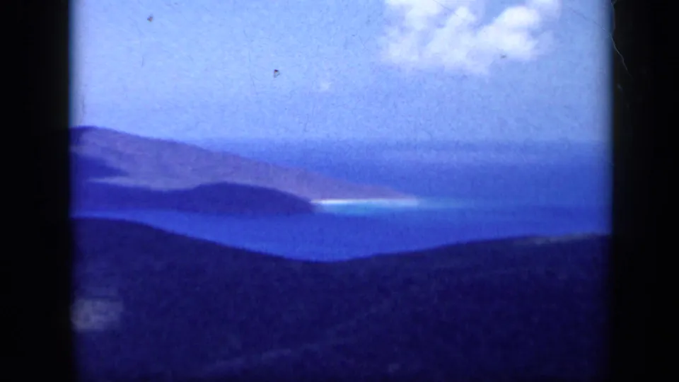 1959 Venezuela 8mm frame showing distant sea, layered headlands or islands, dark foreground hills, and bright clouds above the coast.