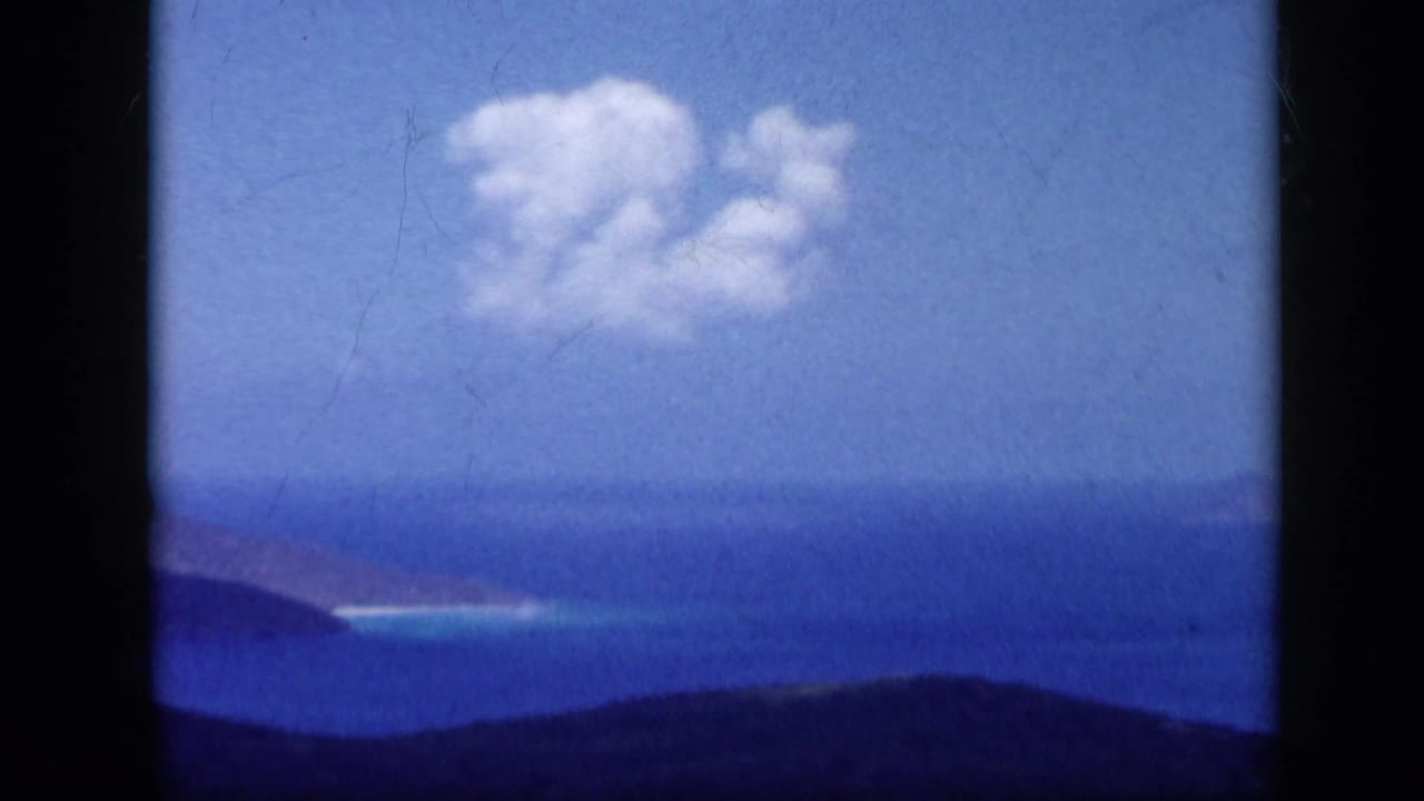 Blue ocean and distant coastline seen beyond dark foreground hills under a clouded sky.