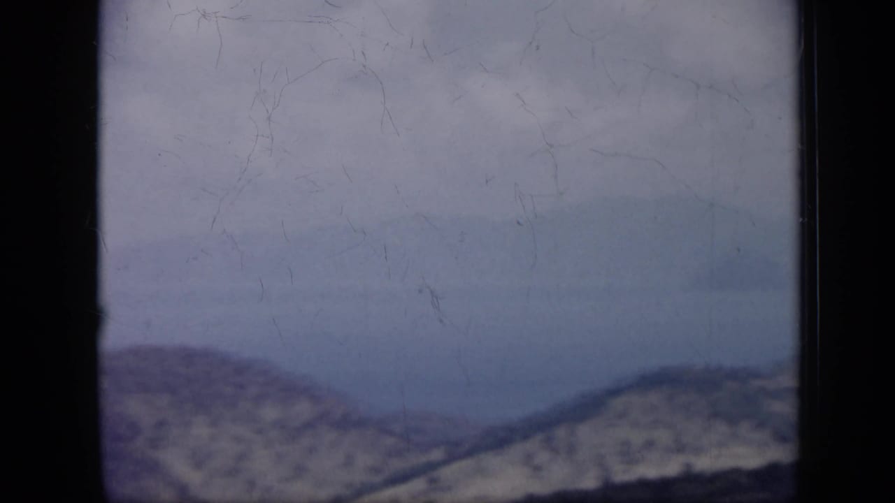 1959 Venezuela 8mm frame with a pale, hazy coastal panorama, distant hills, water, and a bright sky.