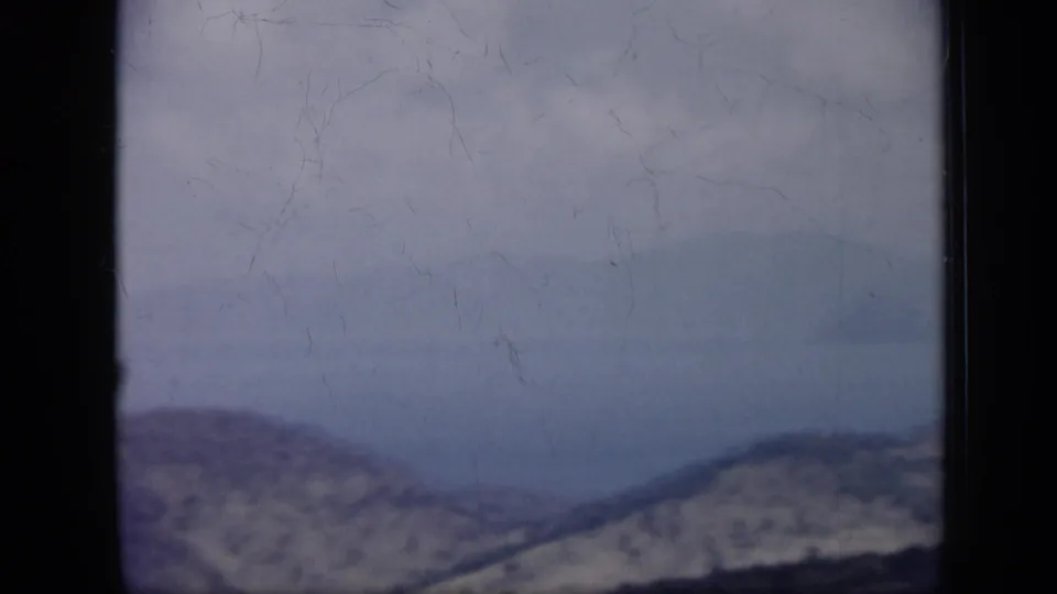 1959 Venezuela 8mm frame with a pale, hazy coastal panorama, distant hills, water, and a bright sky.