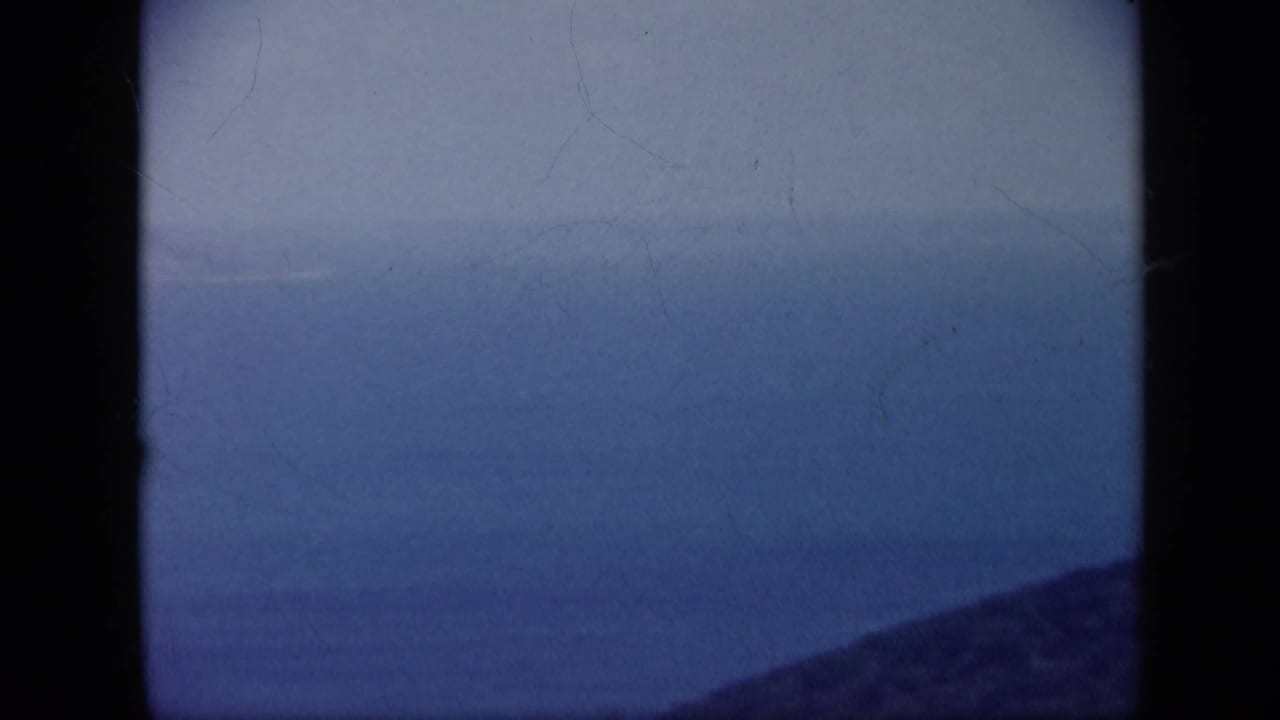 1959 Venezuela 8mm frame looking across blue coastal water toward a faint shoreline, with a dark ridge at the bottom edge.