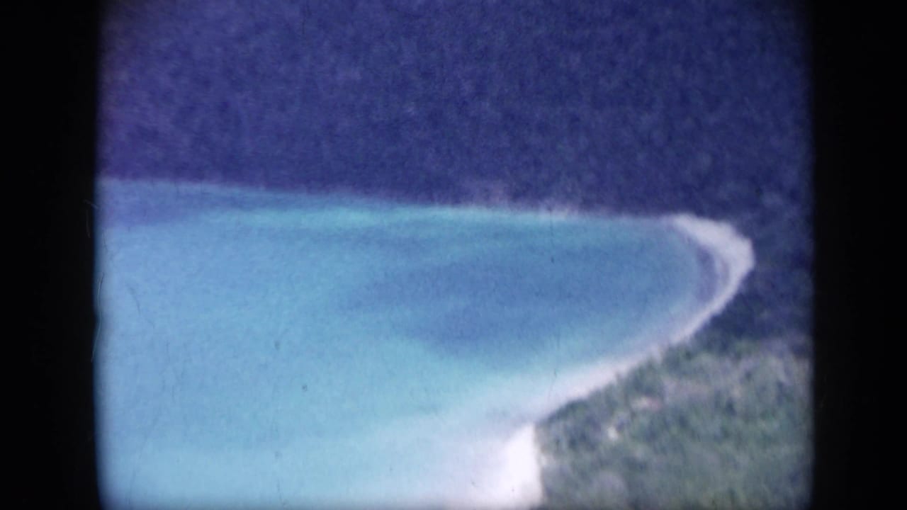 Turquoise bay, pale shoreline, and green coast viewed from above.