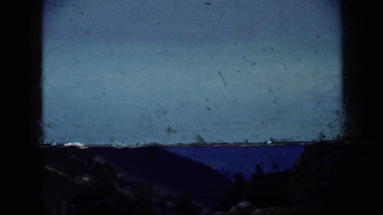 1959 Venezuela 8mm aerial view with blue sea, dark hills, heavy gate shadow, and soft faded color.