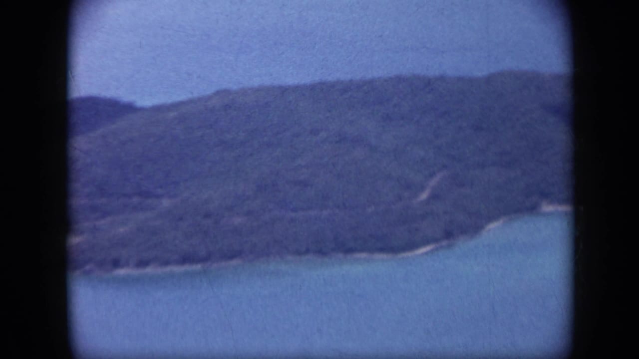 1959 Venezuela aerial view of a green hillside meeting turquoise sea, with soft focus and faded 8mm color.