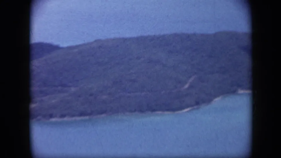1959 Venezuela aerial view of a green hillside meeting turquoise sea, with soft focus and faded 8mm color.