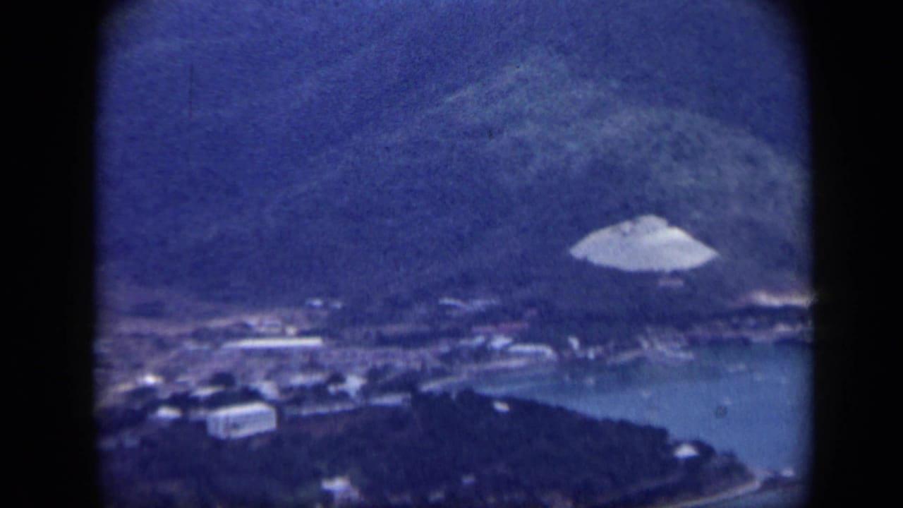 Aerial view of hillside, coastal buildings, harbor water, and a pale hillside structure.