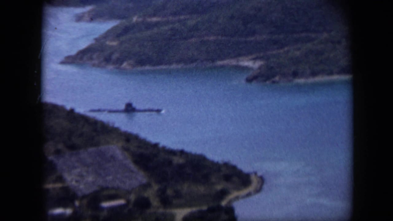 1959 Venezuela aerial frame with coastal water, green shoreline, a road, and a low vessel or submarine-like craft offshore.