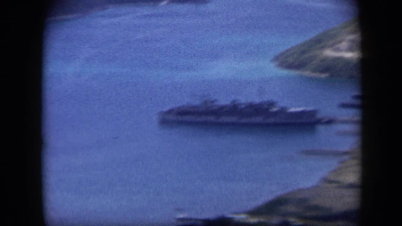 1959 Venezuela 8mm frame showing a large ship moored in blue harbor water beside green island shoreline.