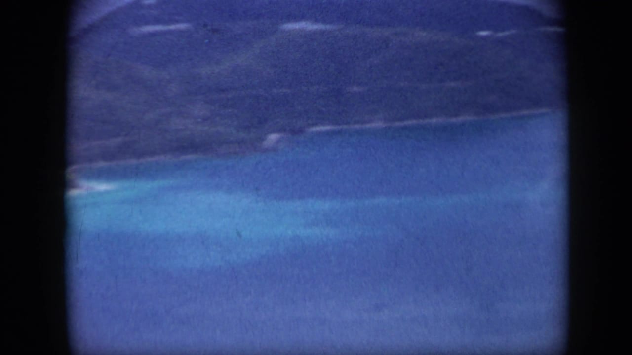 Blue coastal water and green island shoreline seen through dark film borders.