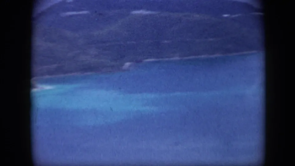 Aerial-looking 1959 Venezuela view of blue water, pale shallows, and green island shoreline within 8mm frame edges.