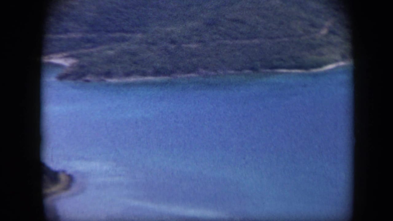 1959 Venezuela 8mm view of a green island edge, bright blue water, and pale shallow areas near shore.