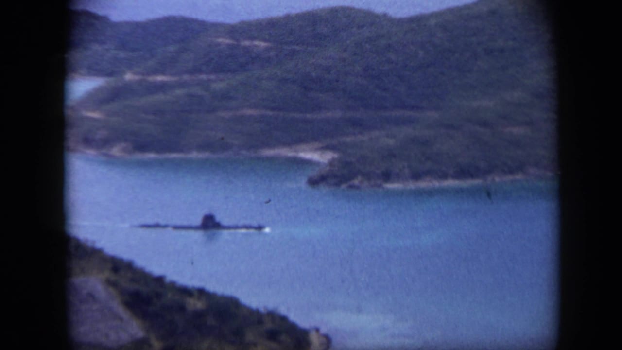 Elevated view of blue water, wooded hills, and a small boat near a shoreline.