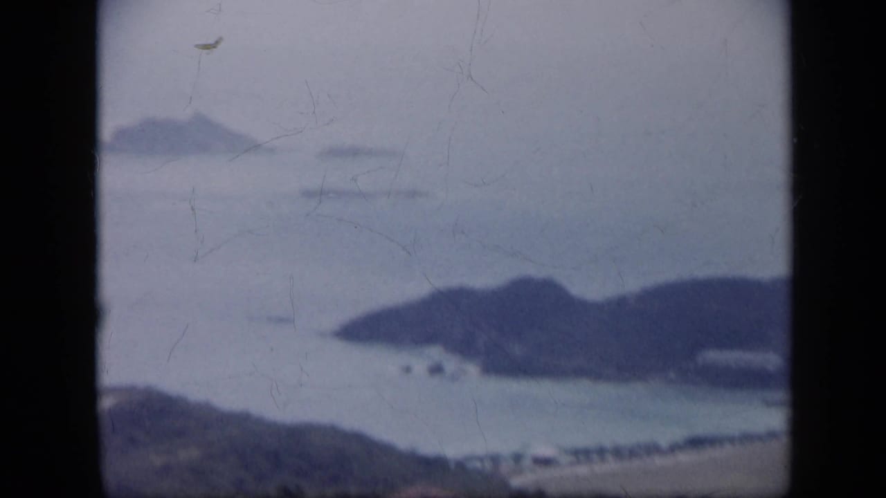 1959 Venezuela 8mm frame showing a hazy coastal bay, dark hills, distant islands, and visible film wear.